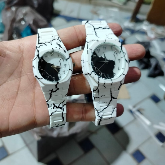 Two white watches with black cracked design on a blurred background